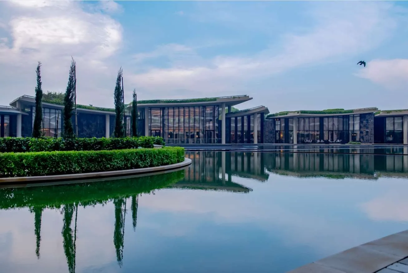 DLF The Camellias — club architecture and landscaped water setting — DLF Hospitality club photograph; membership and access terms apply. Not the offered residence.
